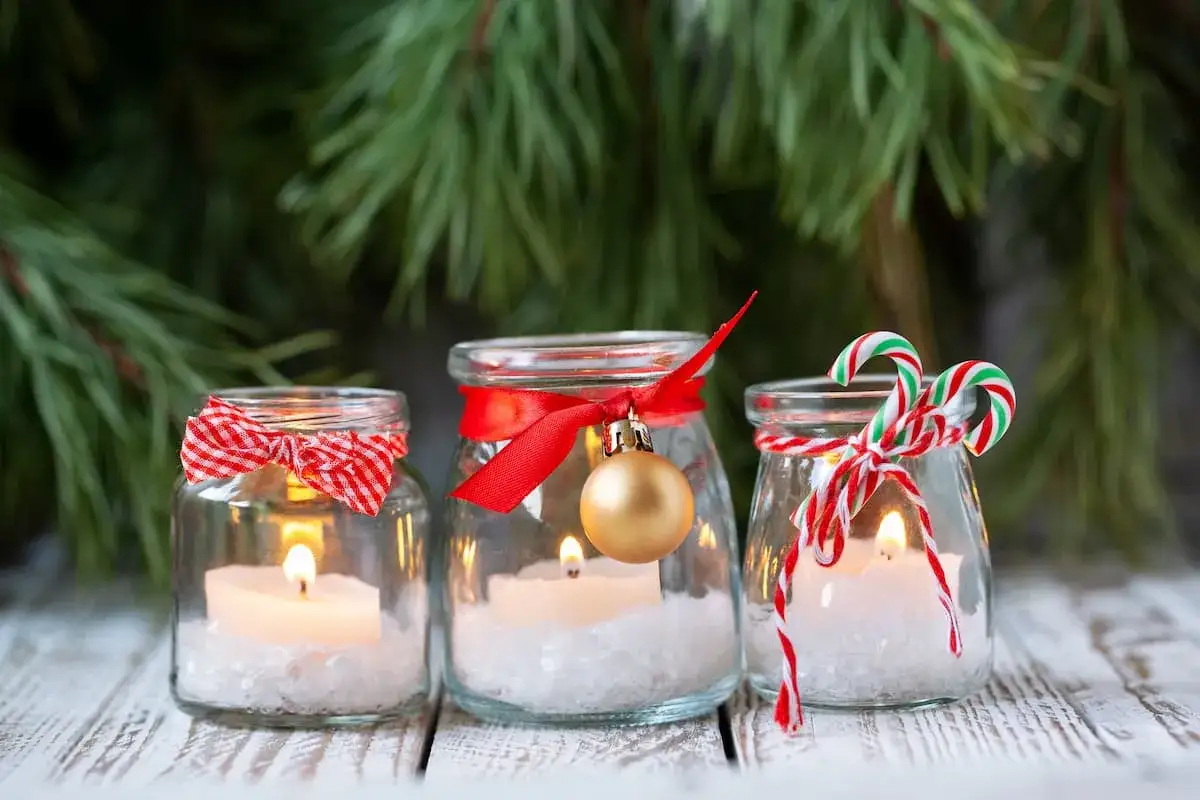 Candele in barattoli decorati con nastri rossi, fiocchi e palline dorate. Perfetti addobbi natalizi fai da te per creare un'atmosfera magica.