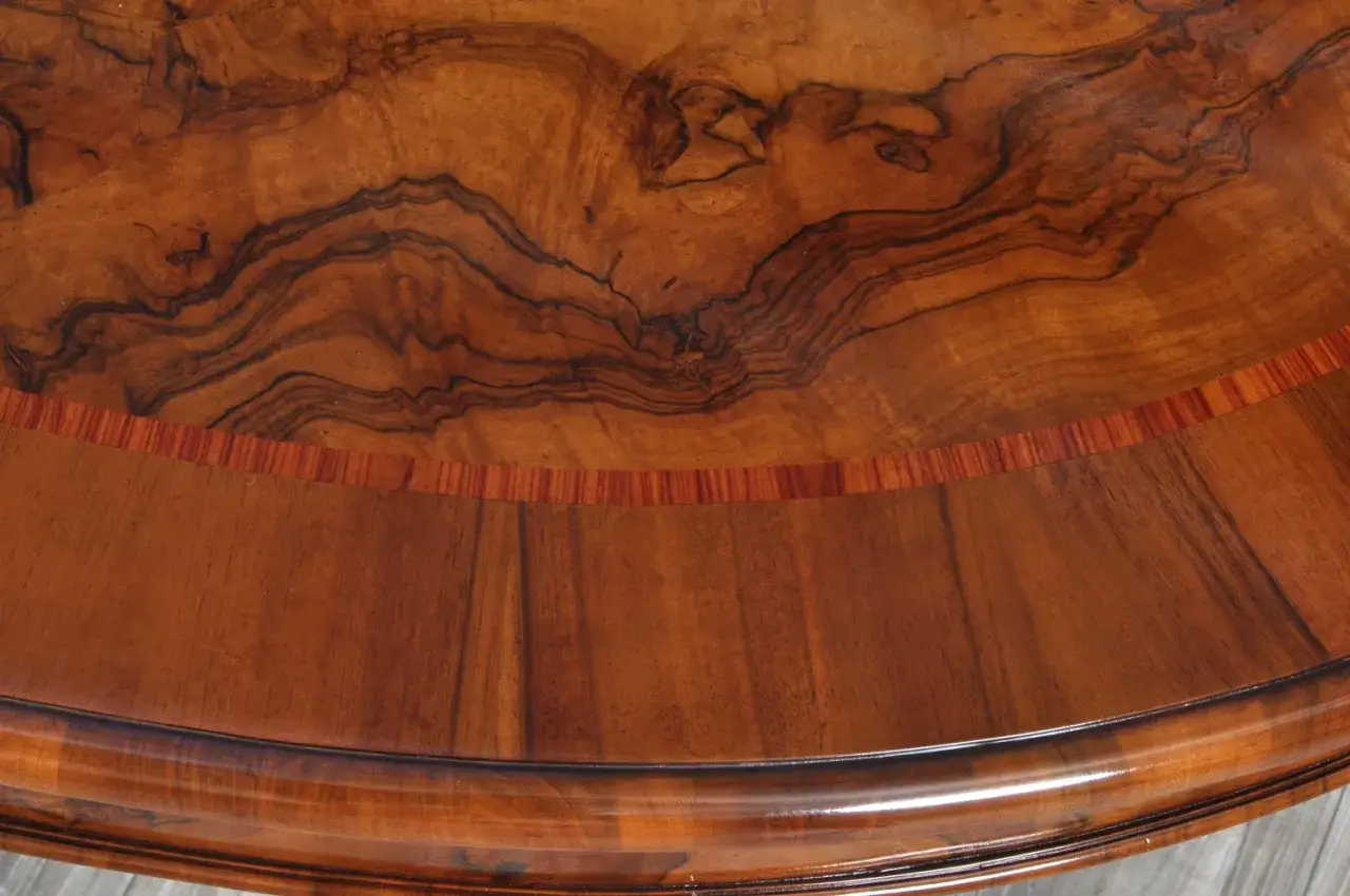 Superficie di un tavolo in legno con venature a radica che creano disegni vorticosi e un bordo intarsiato.