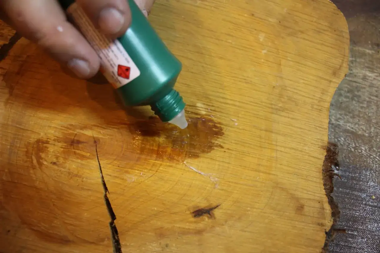 Un flacone verde gocciola un liquido su un tavolo di legno, per rimuovere la colla per unghie.