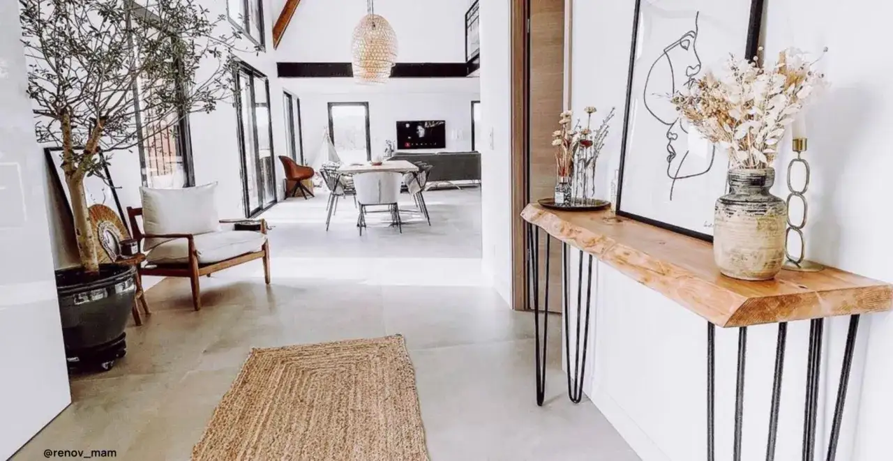 Un'elegante consolle fai da te con piano in legno grezzo e gambe sottili. Un vaso con fiori secchi e un quadro astratto completano l'arredo.