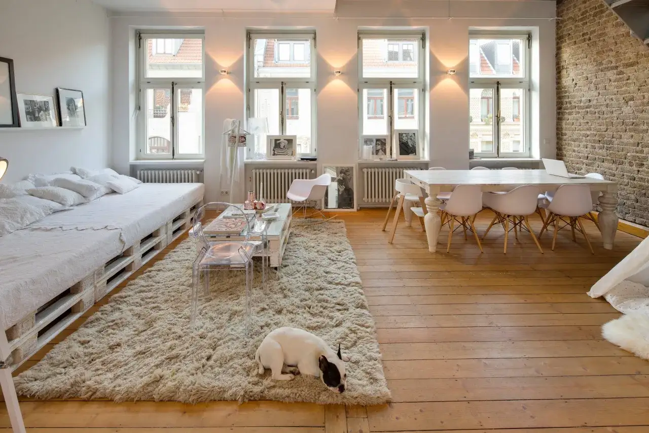 Ampio soggiorno con letto realizzato con bancali, tappeto soffice e un cane bianco e nero. Pareti con bancali e mattoni a vista.
