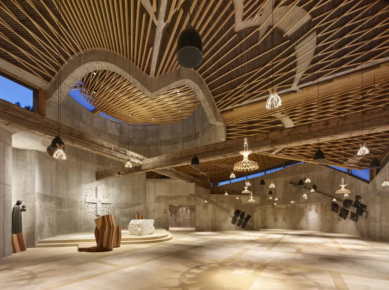 Interno di una chiesa moderna con soffitto in legno a listelli e travi a vista. L'architetto Benedetta Tagliabue ha creato un ambiente suggestivo.