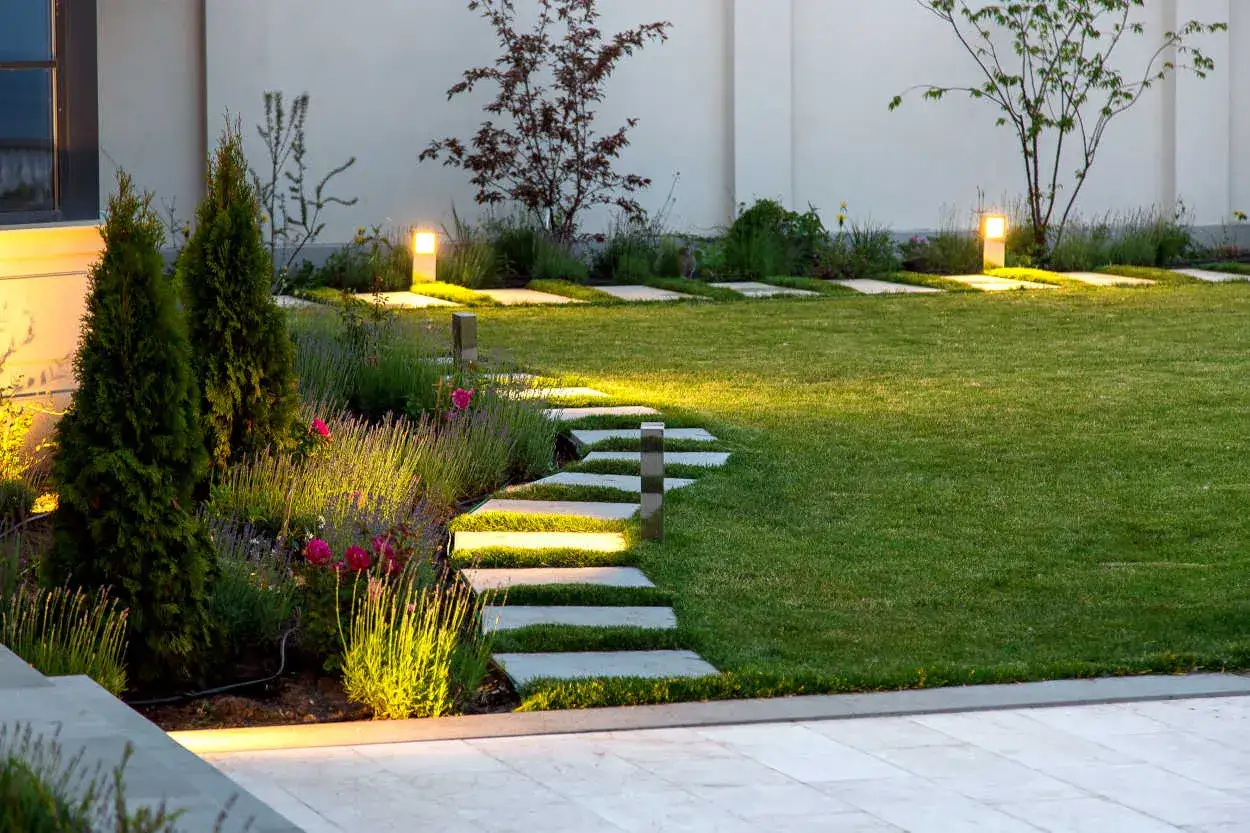 Schema impianto luci giardino: percorso illuminato tra siepi, fiori e prato verde, con faretti che creano un'atmosfera magica.