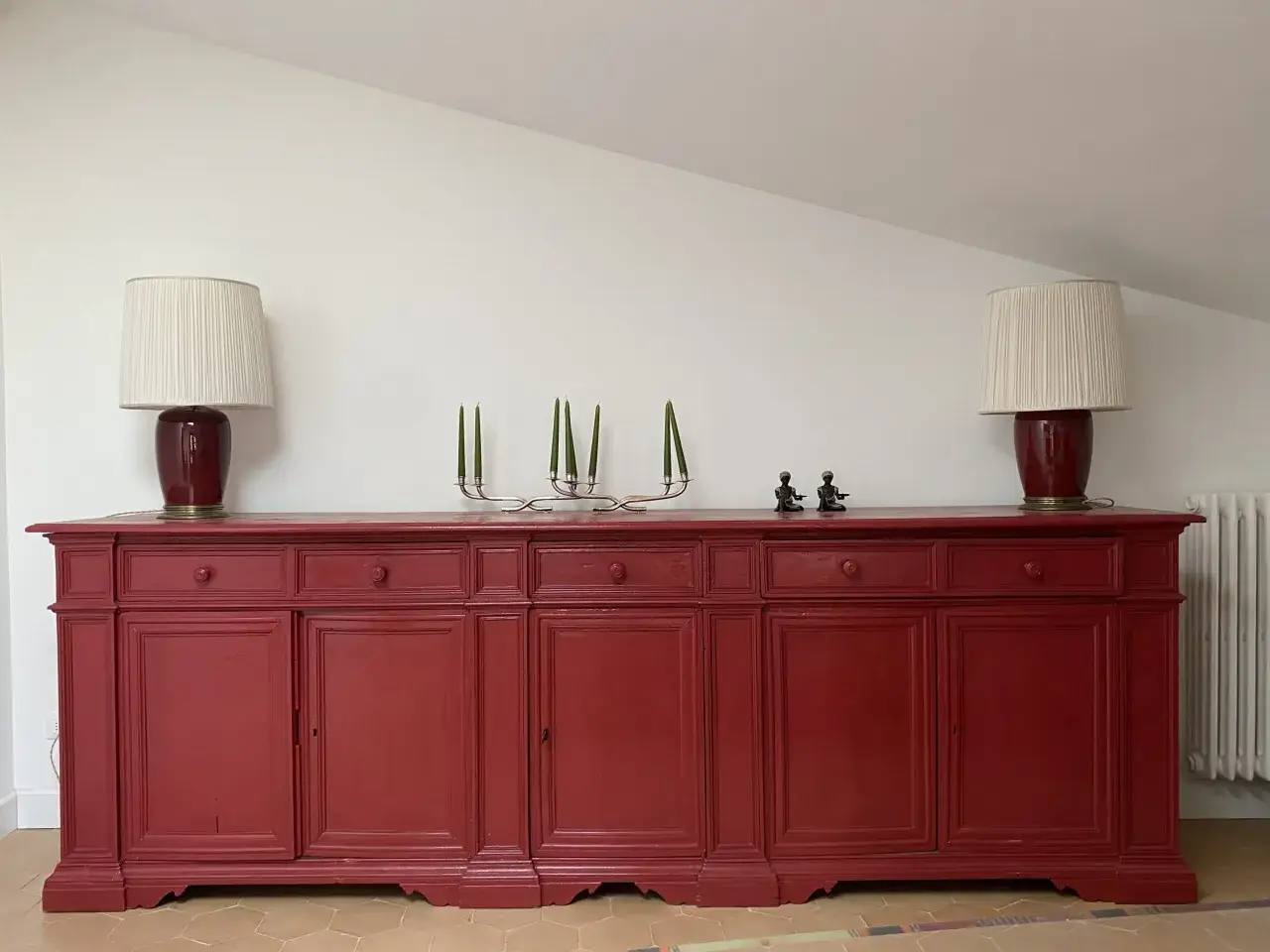 Credenza fai da te rossa, con due lampade, candelabro e statuette.