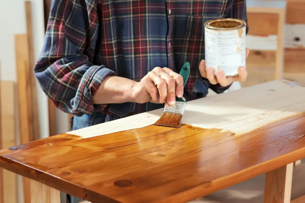 Mano con pennello applica impregnante su legno grezzo, creando una finitura dopo impregnante lucida e calda.