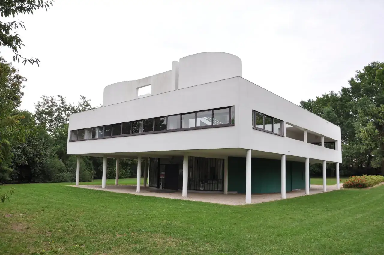 Villa Savoye, capolavoro di Le Corbusier, si erge su pilastri bianchi in un prato verde, con finestre a nastro e una forma curva distintiva.