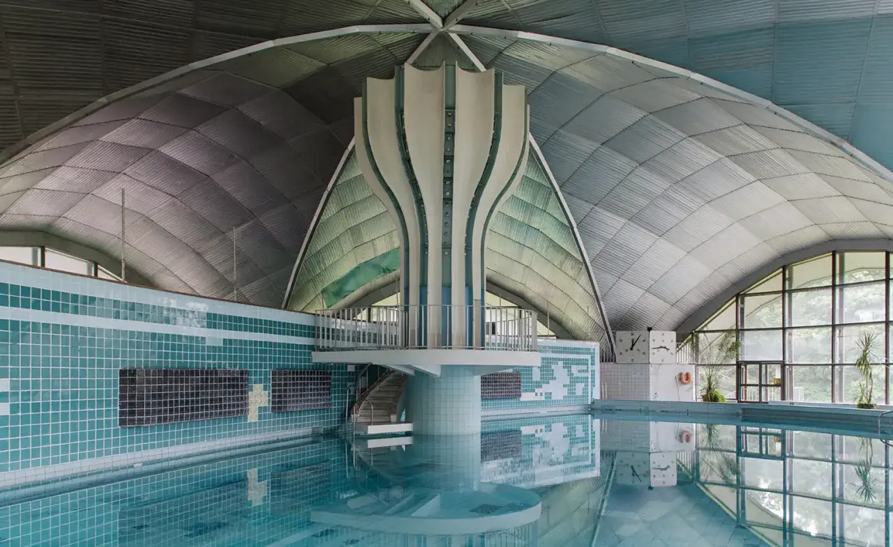 Piscina interna con tetto a volta metallico, piastrelle azzurre e una struttura centrale a forma di fiore. Esempio di brutalismo sovietico.