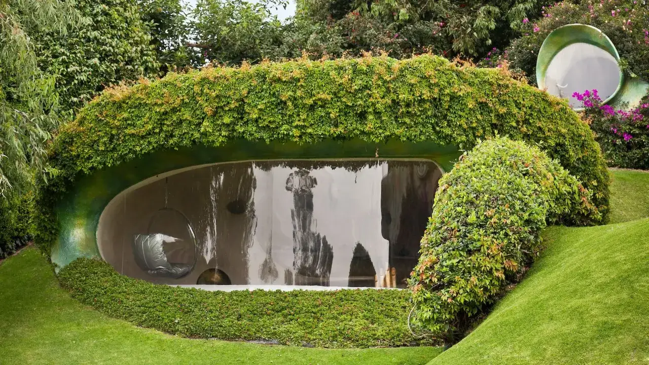 Un esempio di architettura organica: una casa a forma di collina, ricoperta di vegetazione, con un'ampia finestra curva.
