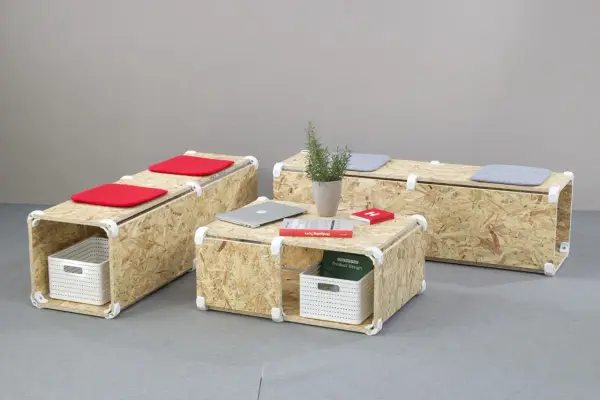 Set di mobili in OSB fai da te: tavolino e panche modulari con cuscini rossi e grigi, cestini portaoggetti e libri.