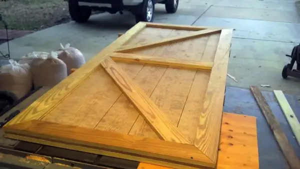 Porta fai da te per esterno in legno grezzo, con rinforzi a X, pronta per essere installata.